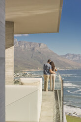 Paar mit Blick auf das sonnige Meer und die Berge vom luxuriösen Balkon - HOXF00159