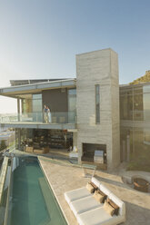 Couple standing on sunny modern luxury home showcase balcony over lap pool - HOXF00161