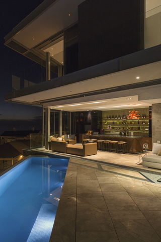 Beleuchtete luxuriöse Hausbar und Terrasse mit Pool bei Nacht, lizenzfreies Stockfoto