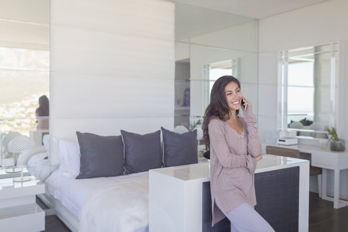Lächelnde Frau, die in einem modernen Luxus-Schlafzimmer mit ihrem Handy telefoniert - HOXF00179