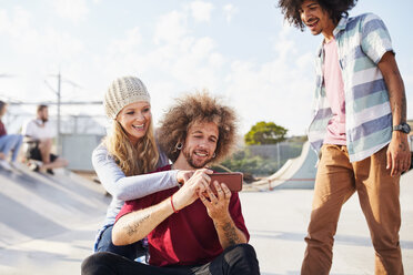 Freunde benutzen ihr Smartphone im sonnigen Skatepark - CAIF04206