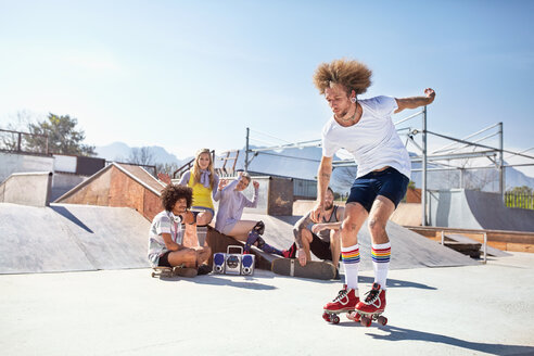 Freunde beobachten Mann beim Rollschuhlaufen im sonnigen Skatepark - CAIF04207