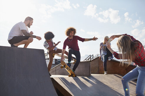 Frau fotografiert männliche Freunde beim Skateboarden auf einer Rampe in einem sonnigen Skatepark - CAIF04215