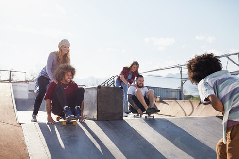 Freunde schieben sich gegenseitig auf Skateboards im sonnigen Skatepark - CAIF04224