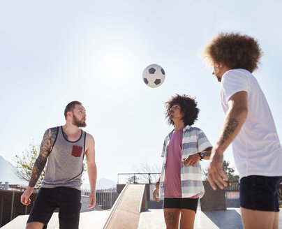 Männliche Freunde spielen Fußball im sonnigen Skatepark - CAIF04226