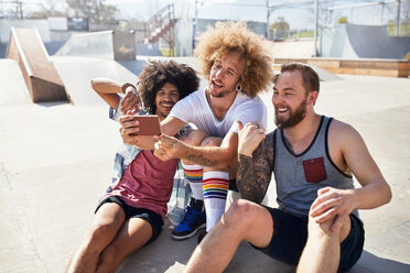 Männliche Freunde mit Fotohandy machen ein Selfie im sonnigen Skatepark - CAIF04227