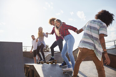 Freunde auf Skateboards halten sich in einer Reihe auf der Rampe im sonnigen Skatepark an den Händen - CAIF04228