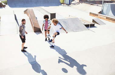 Männliche Freunde spielen Fußball im sonnigen Skatepark - CAIF04234