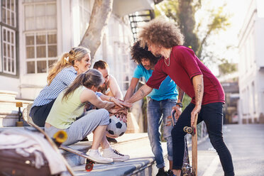 Friends with soccer ball and skateboards touching hands in huddle on urban steps - CAIF04235