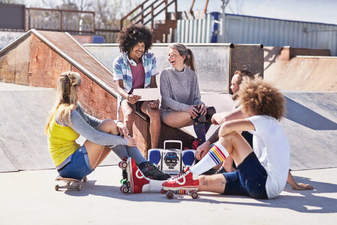 Freunde in Rollschuhen und auf dem Skateboard benutzen ein digitales Tablet in einem sonnigen Skatepark - CAIF04240