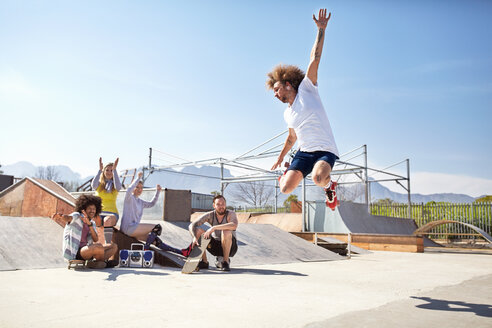 Freunde beobachten und bejubeln einen Mann, der in Rollschuhen in einem sonnigen Skatepark springt - CAIF04245