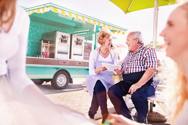 Smiling senior business owners using digital tablet outside food cart - CAIF04250