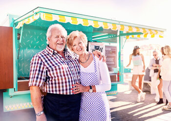 Porträt lächelnder älterer Geschäftsinhaber vor einem sonnigen Imbisswagen - CAIF04251