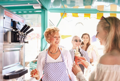 Smiling senior female business owner serving ice cream to young woman at food cart - CAIF04262