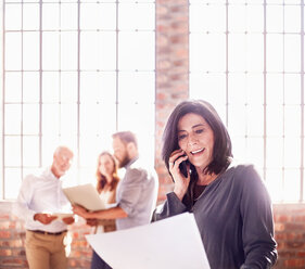 Businesswoman with paperwork talking on cell phone in office - CAIF04263