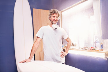 Porträt eines selbstbewussten männlichen Surfbrett-Designers beim Schleifen eines Surfbretts in einer Werkstatt - CAIF04265