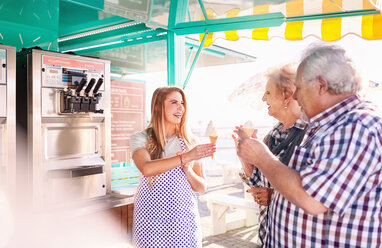 Smiling young woman serving ice cream to senior couple outside food cart - CAIF04276