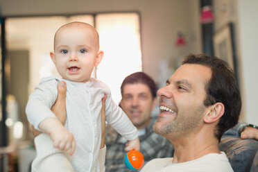 Porträt glücklicher männlicher schwuler Eltern, die ihren kleinen Sohn im Wohnzimmer halten - CAIF04280