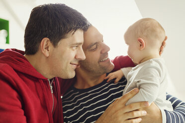 Affectionate male gay parents cuddling baby son - CAIF04288