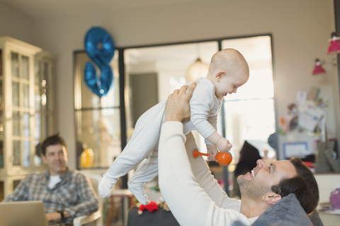 Männliche schwule Eltern spielen mit ihrem kleinen Sohn im Wohnzimmer, lizenzfreies Stockfoto