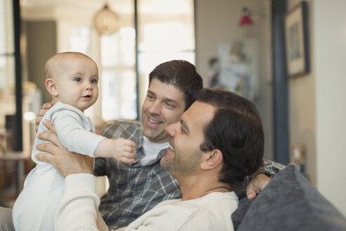 Männliche schwule Eltern halten ihren süßen Babysohn auf dem Sofa - CAIF04291