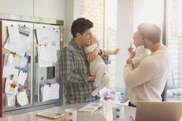 Male gay parents holding baby sons in kitchen - CAIF04298