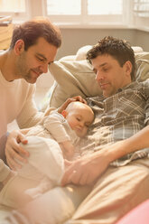 Männliche schwule Eltern beobachten ihren kleinen Sohn beim Schlafen auf dem Sofa - CAIF04335