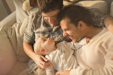 View from above male gay parents cuddling with cute baby son on sofa - CAIF04337