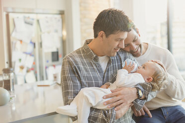 Affectionate male gay parents holding baby son with bottle - CAIF04343