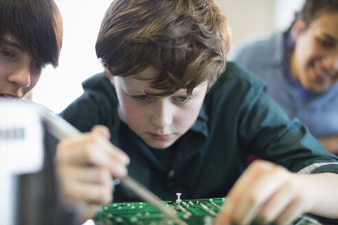 Fokussierter Junge, der im Klassenzimmer Elektronik zusammenbaut - CAIF04357