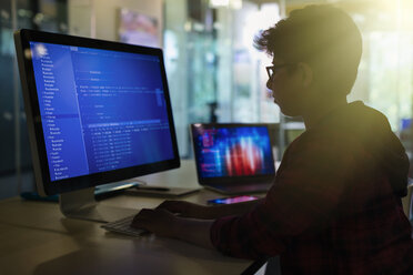 Junge Schülerin beim Programmieren am Computer im dunklen Klassenzimmer - CAIF04372