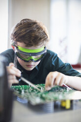 Focused boy student in goggles soldering circuit board in classroom - CAIF04376