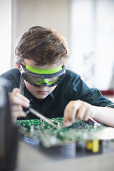 Konzentrierter Schüler mit Schutzbrille beim Löten einer Platine im Klassenzimmer - CAIF04376