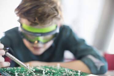 Focused boy student soldering circuit board in classroom - CAIF04377