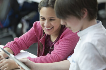 Lächelnde Schüler, die ein digitales Tablet im Klassenzimmer benutzen - CAIF04384