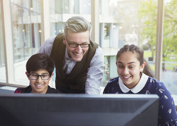 Männlicher Lehrer und Schüler bei der Recherche am Computer in der Bibliothek - CAIF04399