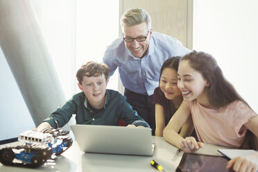 Lächelnder männlicher Lehrer und Schüler, die Roboter am Laptop im Klassenzimmer programmieren - CAIF04404