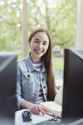 Porträt einer lächelnden, selbstbewussten Studentin, die am Computer in der Bibliothek recherchiert - CAIF04407