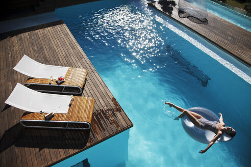 Frau schwimmt auf aufblasbarem Ring in Luxus-Swimmingpool - CAIF04426