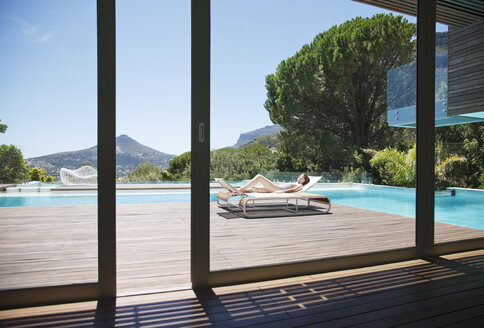 Frau beim Sonnenbaden auf einem Liegestuhl neben einem luxuriösen Swimmingpool mit Blick auf die Berge - CAIF04429