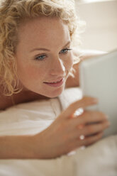 Nahaufnahme einer Frau, die im Bett liegt und ein digitales Tablet benutzt - CAIF04436