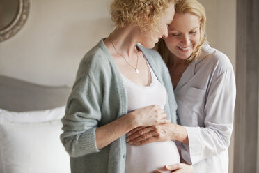 Mother holding pregnant daughter's stomach - CAIF04445