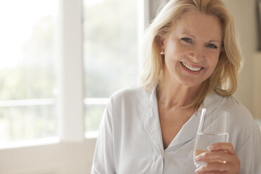 Porträt einer lächelnden Frau, die ein Glas Wasser trinkt - CAIF04451