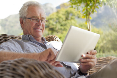Lächelnder älterer Mann mit digitalem Tablet auf der Terrasse - CAIF04459
