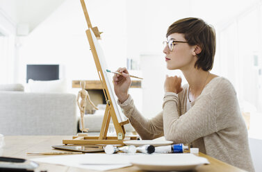 Woman painting on easel at table - CAIF04488