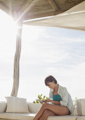 Woman using digital tablet on sunny patio - CAIF04496