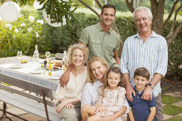 Porträt einer lächelnden Mehrgenerationenfamilie am Tisch im Garten - CAIF04536