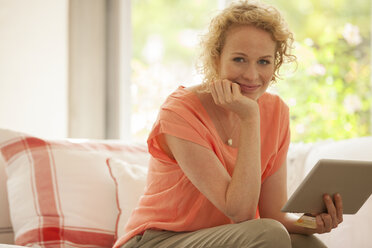 Porträt einer Frau mit digitalem Tablet auf dem Sofa - CAIF04556