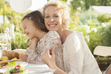 Mother and daughter smiling at table outdoors - CAIF04568