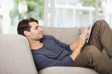 Man using digital tablet on sofa - CAIF04585